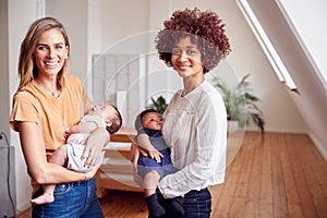 Portrait Of Two Mothers Meeting Holding Newborn Babies At Home In Loft Apartment