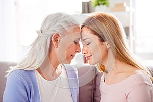 Portrait of two peaceful charming woman sitting sofa closed eyes touch heads house indoors