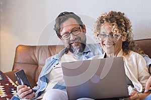 Portrait of two people man and woman enjoy technolofy connection toether with laptop and phone smiling and watching the computer