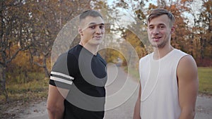 Portrait of two positive Caucasian bodybuilders talking to camera in the autumn park and starting crazy dancing