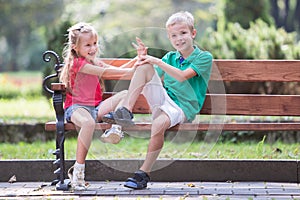 Portrait of two pretty cute children boy and girl having fun time on a bench in summer park outdoors