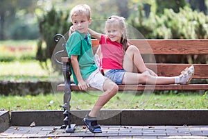 Portrait of two pretty cute children boy and girl having fun time on a bench in summer park outdoors