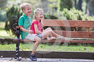 Portrait of two pretty cute children boy and girl having fun time on a bench in summer park outdoors