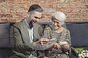 portrait of two relatives bonding and laughing while looking at old vintage photographs that belong to elderly woman