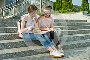 Portrait of two schoolgirls of teenagers with school backpacks and books. Talking, learning