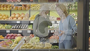 Portrait of two senior Caucasian women walking between rows in grocery and talking. Adult housewives discussing