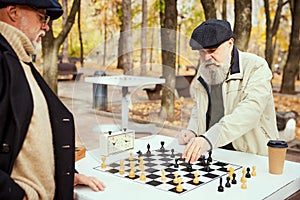 Portrait of two senior men playing chess in the park on a daytime in fall. Buddies hobby. Concept of leisure activity