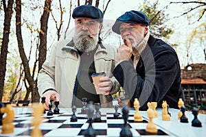 Portrait of two senior men playing chess in the park on a daytime in fall. Concentration. Concept of leisure activity