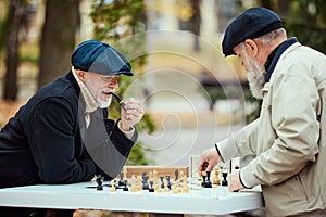 Portrait of two senior men playing chess in the park on a daytime in fall. Game strategy. Concept of leisure activity