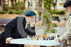 Portrait of two senior men playing chess in the park on a daytime in fall. Hobby. Concept of leisure activity, old