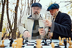 Portrait of two senior men playing chess together in the park on a daytime in fall. Concept of leisure activity, old