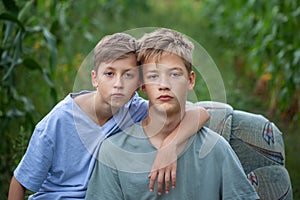 Portrait two serious brothers sitting on a armchair in a field in the countryside in summer day