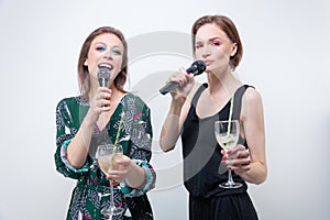 Portrait of two singing girls with glasses in their hands. Karaoke concept