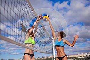 Portrait of two slim sporty girls playing beach volleyball against a bright blue sky