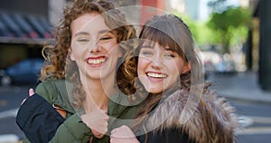 Portrait of two smiling friends hugging and looking happy in the city. Faces of cheerful sisters bonding and having fun