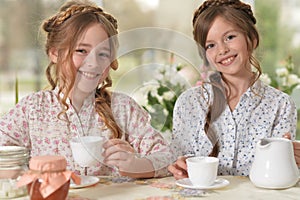 Portrait of two smiling little girls drinking tea at home