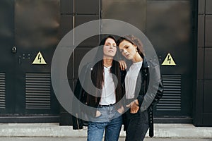 Portrait of two stylish girls in casual clothes posing at camera on black background, wearing leather jackets and jeans. 2