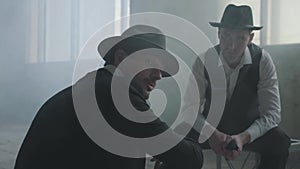 Portrait two stylish men in hats sitting in an abandoned building discussing business. The mafia guys have meeting in an