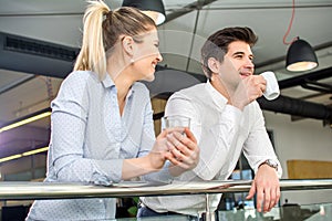 Portrait of two successful business people, man and woman, smiling and talking during coffee break in office building