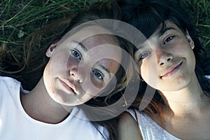 Portrait of two teen girls friends lying on the grass, close-up shot from above.