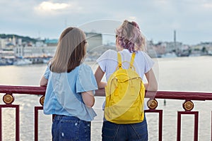 Portrait of two teenage girls standing with their backs on bridge over river