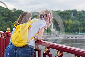 Portrait of two teenage girls standing with their backs on bridge over river
