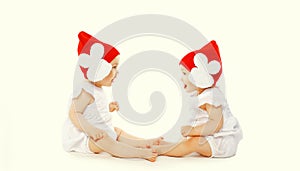 Portrait of two twin babies looking at each other wearing red winter knitted hats playing on white background