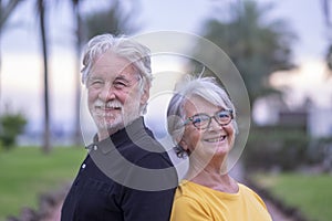 Portrait of two white-haired senior people smiling happily during retirement. Standing outdoors in a public park back to back
