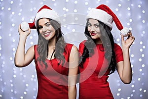 Portrait of two women in santa hats and red dress on bokeh light background. Winter holiday Christmas and New Year concept