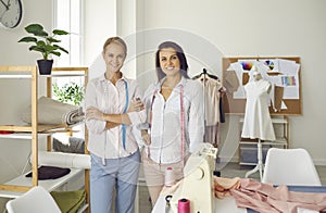 Portrait of two women seamstresses working in sewing workshop and standing near their workplace.