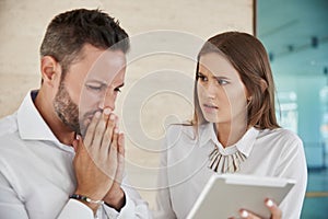 Two worried coworkers working together on tablet