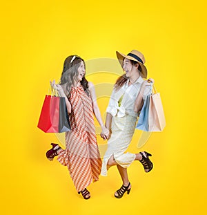 Portrait of two young asian women in casual beach clothing with credit card and shopping bag on sale promotion isolated on yellow