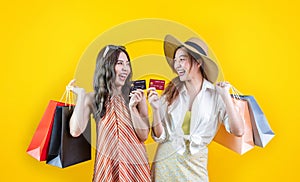 Portrait of two young asian women in casual beach clothing with credit card and shopping bag on sale promotion isolated on yellow