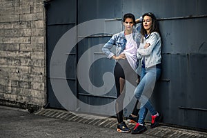 Portrait of two young and attractive women standing next to the wall.