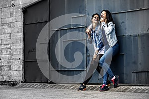 Portrait of two young and attractive women standing next to the wall.