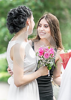 Portrait of two young beautiful women friends talking in green summer park. Pretty females Bride and bridesmaid smiling hugging an