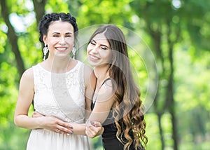 Portrait of two young beautiful women laughing and hugging each other in green summer park. Pretty females bride and bridesmaid sm