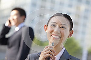 Portrait of two young business people holding phone, outside in the business district, Beijing