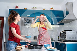 Portrait of two young Caucasian women cook pizza in the kitchen and have fun together. Indoors. Concept of family