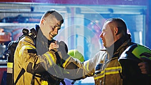 Portrait of two young firefighters on the rain in front of fire engine in full uniform. Fire dril