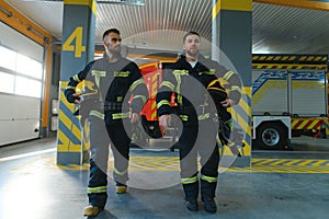 Portrait of two young firemen in uniform standing inside the fire station