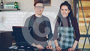 Portrait of two young good-looking waiters standing at cashier's desk in coffee-house and smiling. Successful