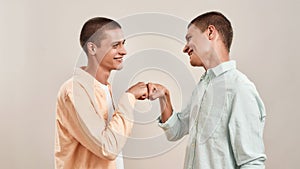 Portrait of two young happy twin brothers looking at each other and giving fist bump while standing face to face