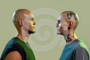 Portrait of two young men, twin brothers with tattoos and piercings looking at each other, posing together, standing