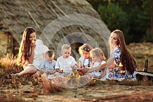 Portrait of a two young mothers with pleasure spending time with her four precious kids on picnic in the summer park