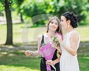 Portrait of two young pretty women friends talking in green summer park. Pretty females bride and bridesmaid smiling and chatting