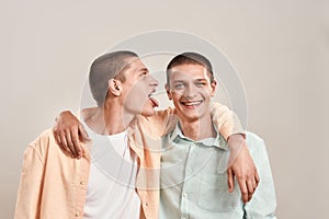 Portrait of two young twin brothers hugging and having fun while posing together isolated over beige background