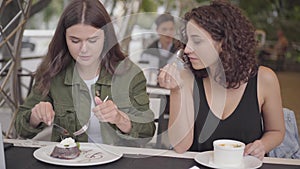 Portrait of two young women eating a cake sitting in cafe outdoors. Young girls together enjoying their meal talking