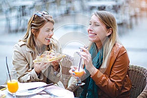 Portrait of two young women eating pizza outdoors