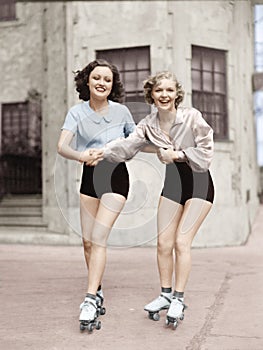 Portrait of two young women with roller blades skating on the road and smiling